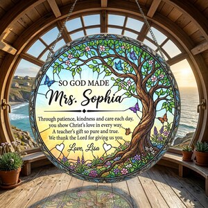 May include: A circular stained glass suncatcher featuring a tree with green leaves, pink flowers, and colorful butterflies. The text reads: SO GOD MADE Mrs. Sophia. Through patience, kindness and care each day, you show Christ's love in every way. A teacher's gift so pure and true. We thank the Lord for giving us you. Love, Lisa.