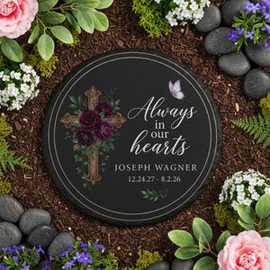 May include: A round, black memorial stone with the text "Always in our hearts" and the name "Joseph Wagner" with dates. The stone features a cross adorned with burgundy flowers and a butterfly graphic.