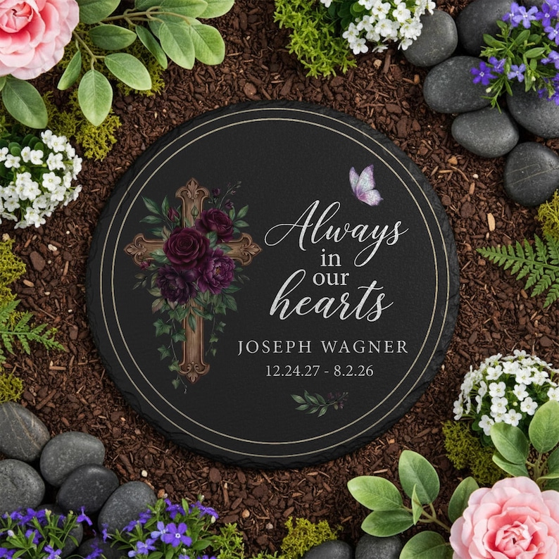 May include: A round, black memorial stone with the text "Always in our hearts" and the name "Joseph Wagner" with dates. The stone features a cross adorned with burgundy flowers and a butterfly graphic.