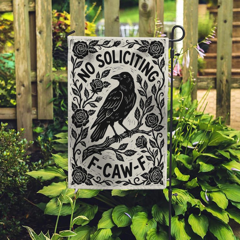 K&ouml;nnte beinhalten: Eine schwarz-wei&szlig;e Gartenflagge mit einer Rabenillustration auf einem Ast, umgeben von Rosen und den Worten "NO SOLICITING" und "F-CAW-F". Die Flagge wird im Freien in einem Garten gezeigt.