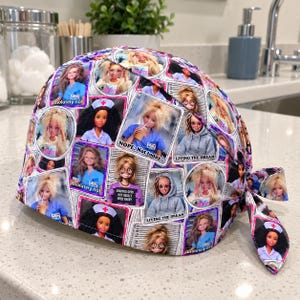May include: A scrub cap featuring a repeating pattern of doll portraits in various outfits and poses. Text on the fabric includes phrases like absolutely not, NOPE. Not today, and LIVING THE DREAM. The cap has a tie-back closure and a colorful print.