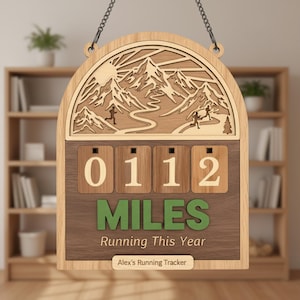 May include: Wooden running tracker with a mountain scene and the text "0112 MILES Running This Year." The tracker has a chain for hanging and a small nameplate that says "Alex's Running Tracker."