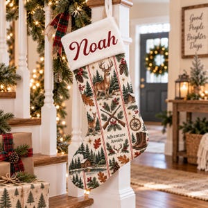 Puede incluir: Un calcetín navideño con un puño blanco que muestra el nombre Noah en letra roja. El cuerpo presenta un patrón de rayas verticales con ilustraciones de un ciervo, pinos, rifles cruzados, una brújula, botas y el texto Adventure Awaits.