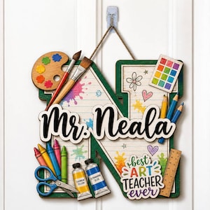 May include: A wooden letter N wall sign featuring the name Mr. Neala and the text best ART TEACHER ever. The sign is decorated with colorful paint splatters, a palette, brushes, crayons, scissors, paint tubes, a ruler, and a watercolor set.
