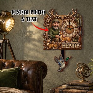 May include: A wooden wall clock with a hunting theme. The clock face features a man, deer, and a rifle. The clock has the name "HENRY" and the text "CUSTOM PHOTO & TEXT". A decorative duck hangs below the clock.