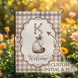 May include: A garden flag featuring a watercolor illustration of a cat, the letter "K" made of paw prints, and the word "Welcome". The flag has a brown and white checkered background and a decorative border. The text "CUSTOM INITIAL & PETS" is also visible.
