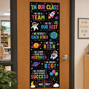 May include: A vertical black classroom door banner featuring colorful space-themed graphics and text including IN OUR CLASS WE ARE A TEAM, WE TRY OUR BEST, WE RESPECT EACH OTHER, WE TAKE RISK, WE LEARN FROM OUR MISTAKES, WE DREAM BIG, WE CELEBRATE EACH OTHERS SUCCESS, MRS. EMILY.