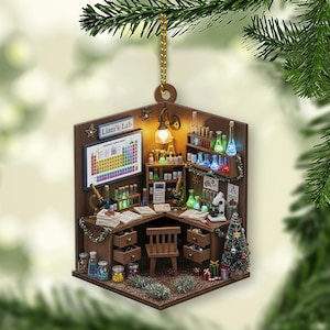 以下が含まれることがあります： 「Liam's Lab」の文字と周期表が描かれた、実験室を模したミニチュアのクリスマスオーナメント。顕微鏡、試験管、小さなクリスマスツリーが特徴です。オーナメントは茶色で、金色の紐で吊り下げられています。