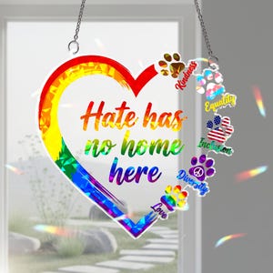 以下が含まれることがあります： 虹色のデザインと「Hate has no home here」の文字が入ったハート型のサンキャッチャー。 「Kindness」、「Equality」、「Inclusion」などの言葉が入った足跡も特徴です。 サンキャッチャーはチェーンから吊り下げられています。