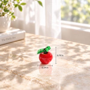 May include: A miniature red glass apple figurine with a green glass leaf. The apple measures 0.59 inches in width and 0.79 inches in height, as indicated by the visible measurement lines and text labels on the image.