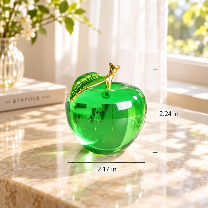 May include: A translucent green glass apple figurine featuring a polished gold-tone metal stem and leaf. The apple measures 2.17 inches in width and 2.24 inches in height, showcasing a smooth, reflective surface that catches the light.