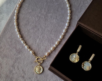 Peut inclure: Un collier de perles blanches avec un pendentif soleil en or et des boucles d'oreilles assorties. Le collier a un fermoir à glissière. Les bijoux sont présentés sur un fond en velours gris et dans une boîte en velours marron.