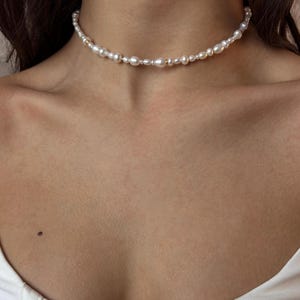 May include: A delicate pearl choker necklace with small, irregular pearls. The necklace is made of gold-toned metal and features a simple, elegant design.