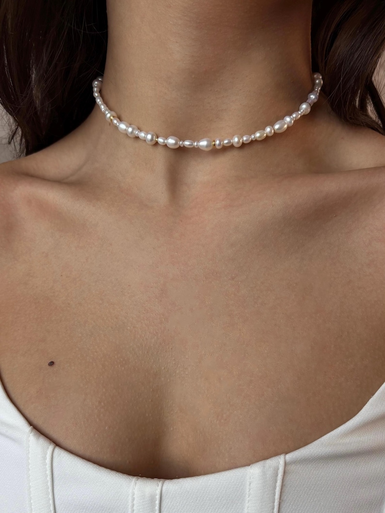 May include: A delicate pearl choker necklace with small, irregular pearls. The necklace is made of gold-toned metal and features a simple, elegant design.