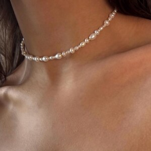 May include: A delicate pearl choker necklace with small, white pearls and gold accents.