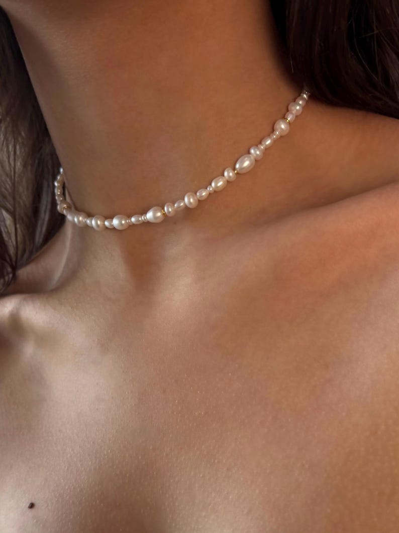 May include: A delicate pearl choker necklace with small, white pearls and gold accents.