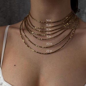 May include: A collection of gold-colored necklaces of varying lengths, ranging from 14 inches to 22 inches. Each necklace is displayed layered on top of each other, with the length of each necklace clearly labeled in inches.