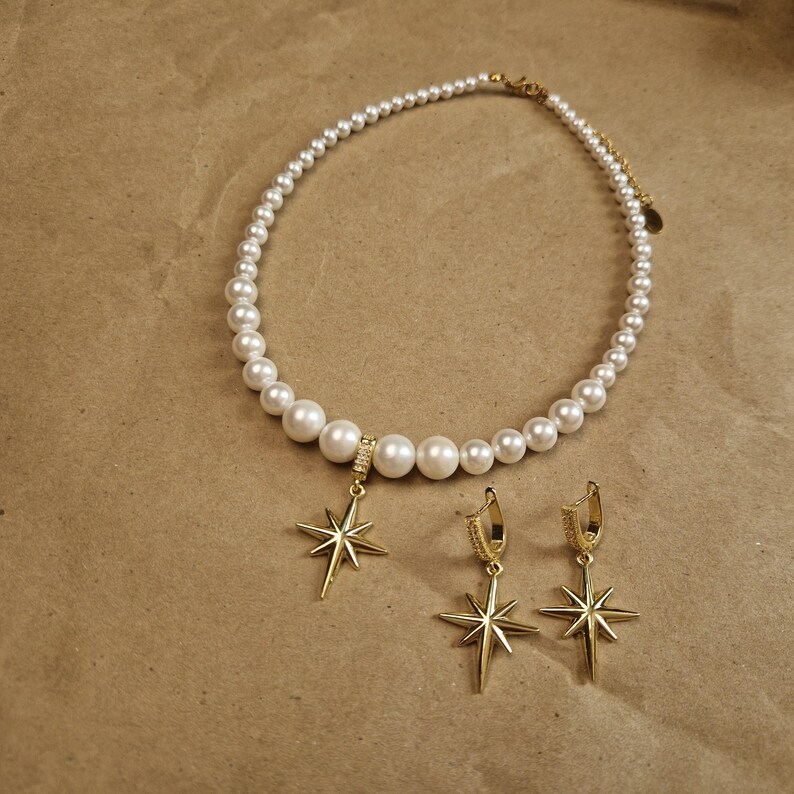 May include: A pearl necklace and matching earrings set. The necklace features white pearls of varying sizes, with a gold-colored clasp. The earrings and pendant are gold-colored starburst designs, with small clear stones.