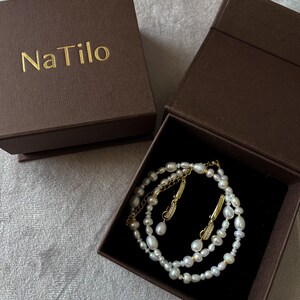 May include: A set of pearl earrings and a pearl necklace in a brown box with the text "Na Tilo" on the lid.