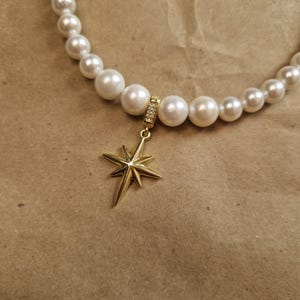 May include: A pearl necklace with a gold star pendant. The necklace features large, round, white pearls. The star pendant is gold-colored and has a multi-pointed design. The pendant's bail is adorned with small, clear crystals.