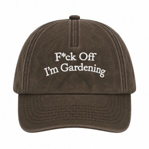 Peut inclure: Une casquette de baseball marron fonc&eacute; avec une finition d&eacute;lav&eacute;e et us&eacute;e. L'avant pr&eacute;sente un texte brod&eacute; en blanc qui indique F*ck Off I'm Gardening dans une police sans empattement. La casquette a une calotte structur&eacute;e et une visi&egrave;re courb&eacute;e.