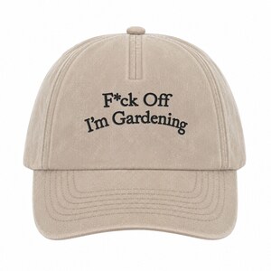 Peut inclure: Une casquette de baseball beige avec une construction &agrave; six panneaux et une visi&egrave;re incurv&eacute;e. L'avant pr&eacute;sente un texte brod&eacute; en noir qui indique F*ck Off I'm Gardening dans une police sans empattement. La casquette a un bouton sur le dessus.