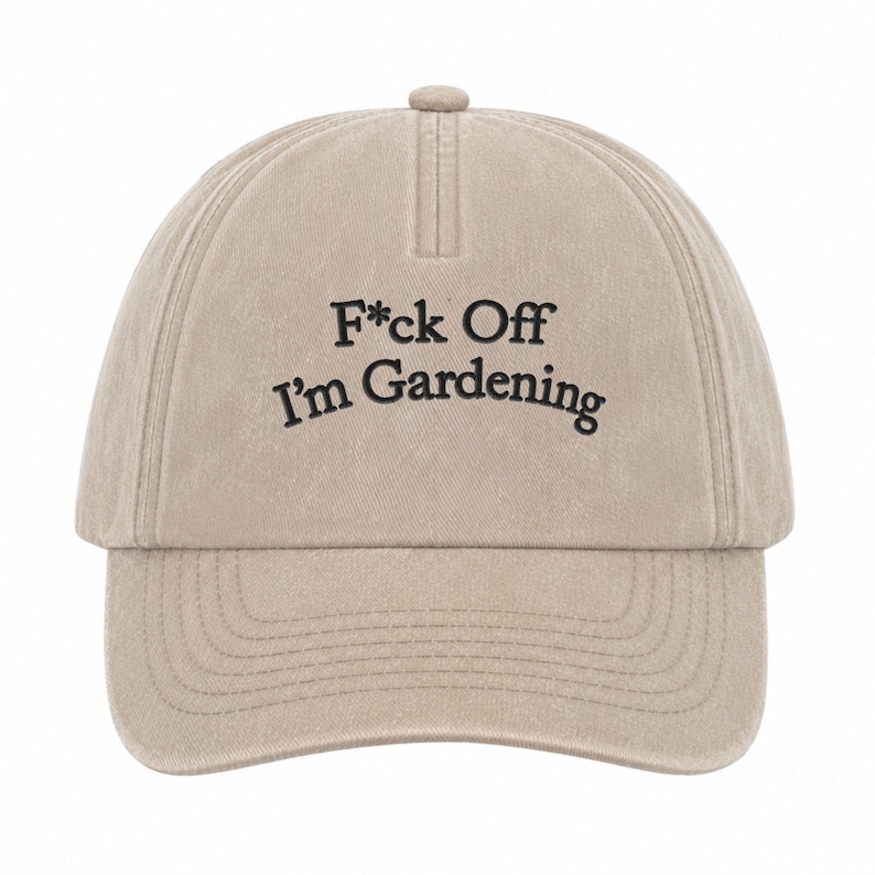 Peut inclure: Une casquette de baseball beige avec une construction &agrave; six panneaux et une visi&egrave;re incurv&eacute;e. L'avant pr&eacute;sente un texte brod&eacute; en noir qui indique F*ck Off I'm Gardening dans une police sans empattement. La casquette a un bouton sur le dessus.