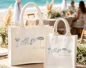 May include: Two cream canvas tote bags with matching handles. Each bag features a light blue illustration of beach-themed icons and the text "J & S. Prod" and "2023". The bags are on a table with a beach backdrop.