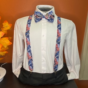 May include: A white button-down shirt with a bow tie and suspenders. The bow tie and suspenders are patterned with an American flag and the word "Navy".