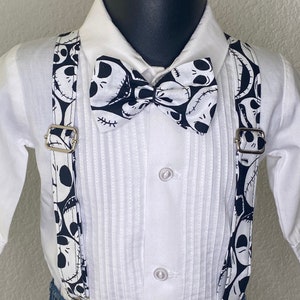 May include: A white button-down shirt with a black and white bow tie and suspenders. The bow tie and suspenders feature a pattern of Jack Skellington's face from the Nightmare Before Christmas.