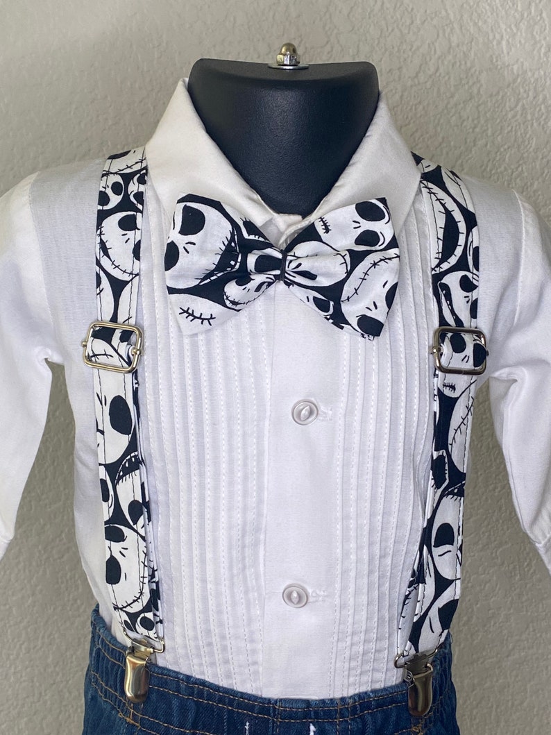 May include: A white button-down shirt with a black and white bow tie and suspenders. The bow tie and suspenders feature a pattern of Jack Skellington's face from the Nightmare Before Christmas.