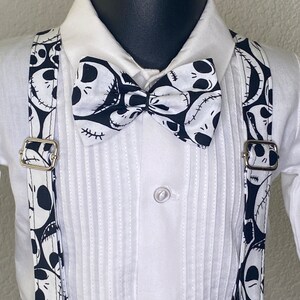 May include: A white button-down shirt with a black bow tie and suspenders. The bow tie and suspenders feature a black and white pattern of Jack Skellington's face from The Nightmare Before Christmas.