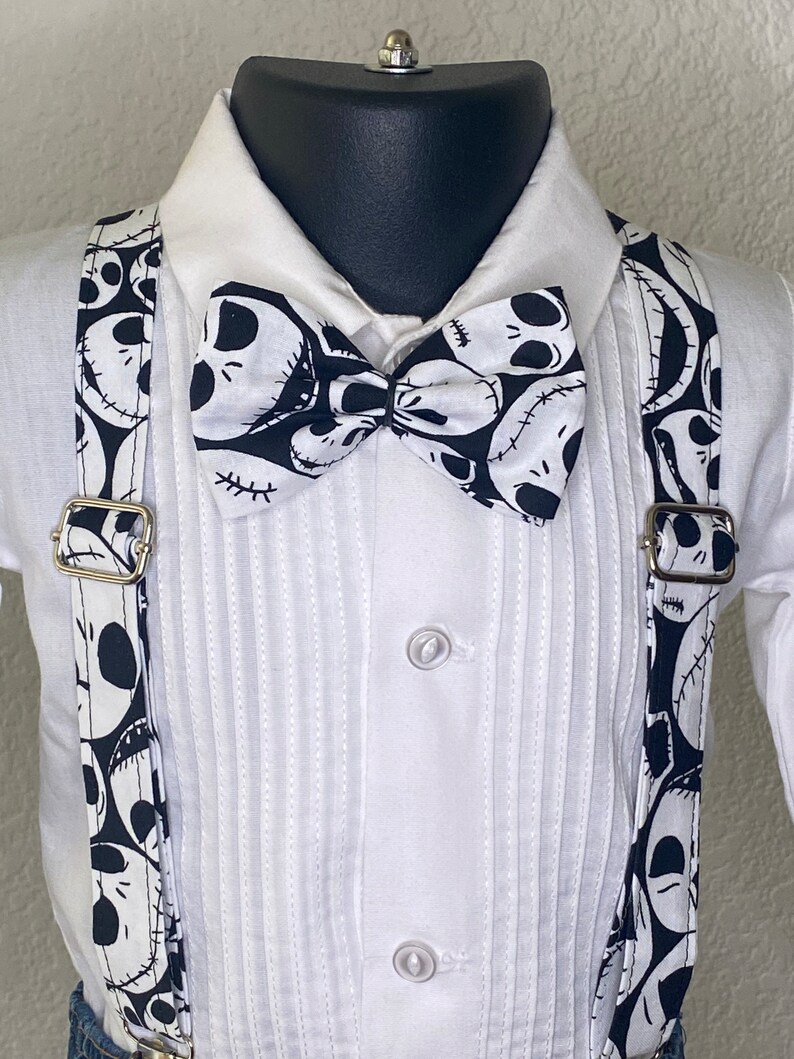 May include: A white button-down shirt with a black bow tie and suspenders. The bow tie and suspenders feature a black and white pattern of Jack Skellington's face from The Nightmare Before Christmas.