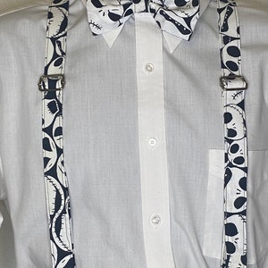May include: White button-down shirt with black and white suspenders and a black and white bow tie featuring a repeated pattern of Jack Skellington's face from the Nightmare Before Christmas.