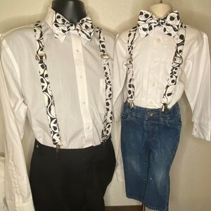 May include: Two white button-down shirts with black and white bow ties and suspenders featuring a pattern of Jack Skellington's face from the Nightmare Before Christmas. The shirt on the left is paired with black pants, while the shirt on the right is paired with blue jeans.