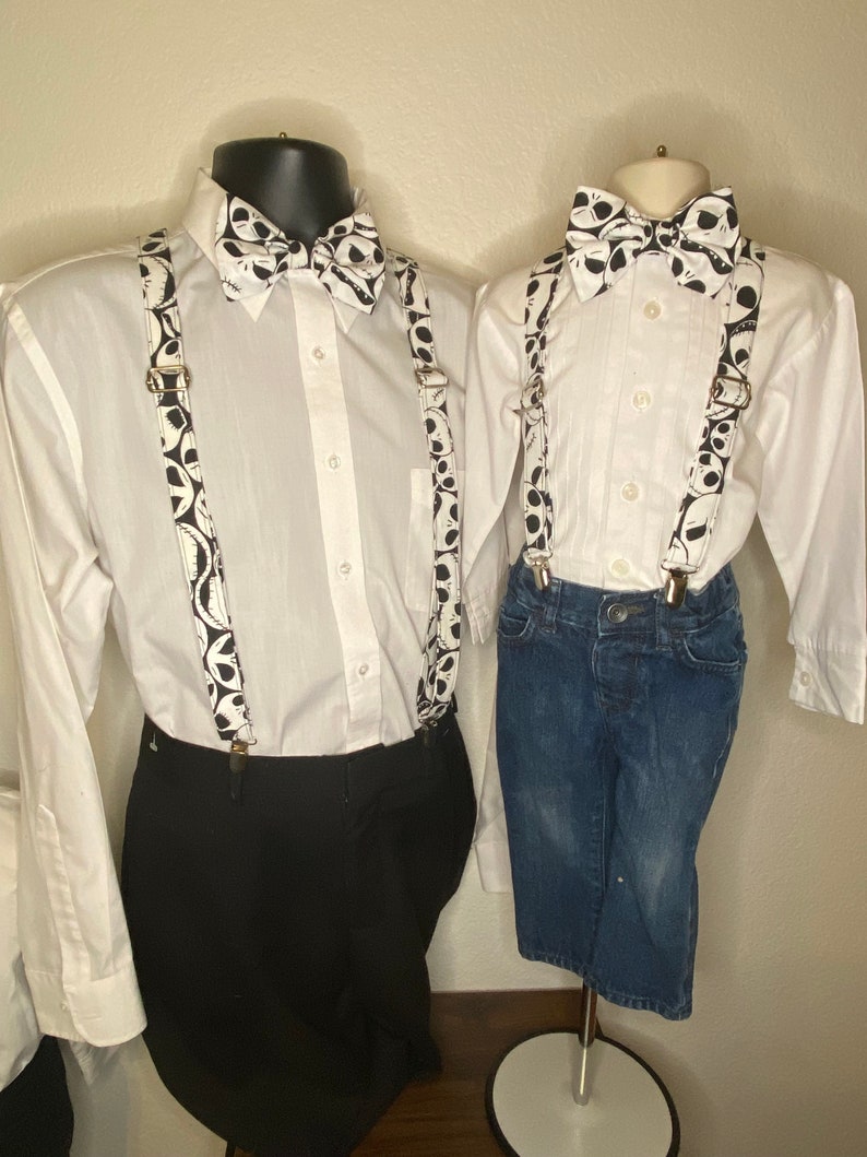 May include: Two white button-down shirts with black and white bow ties and suspenders featuring a pattern of Jack Skellington's face from the Nightmare Before Christmas. The shirt on the left is paired with black pants, while the shirt on the right is paired with blue jeans.