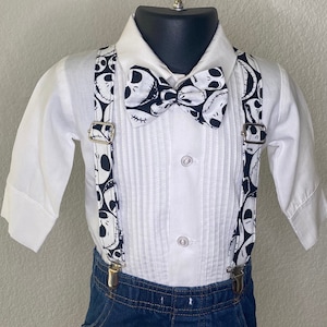 May include: A white button-down shirt with a black and white bow tie and suspenders. The bow tie and suspenders feature a pattern of Jack Skellington's face from the movie The Nightmare Before Christmas.