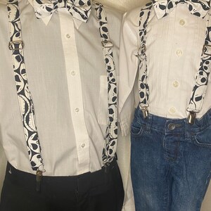 May include: Two white button-down shirts with black and white bow ties and suspenders featuring a Jack Skellington pattern. The suspenders are attached to black pants and blue jeans.