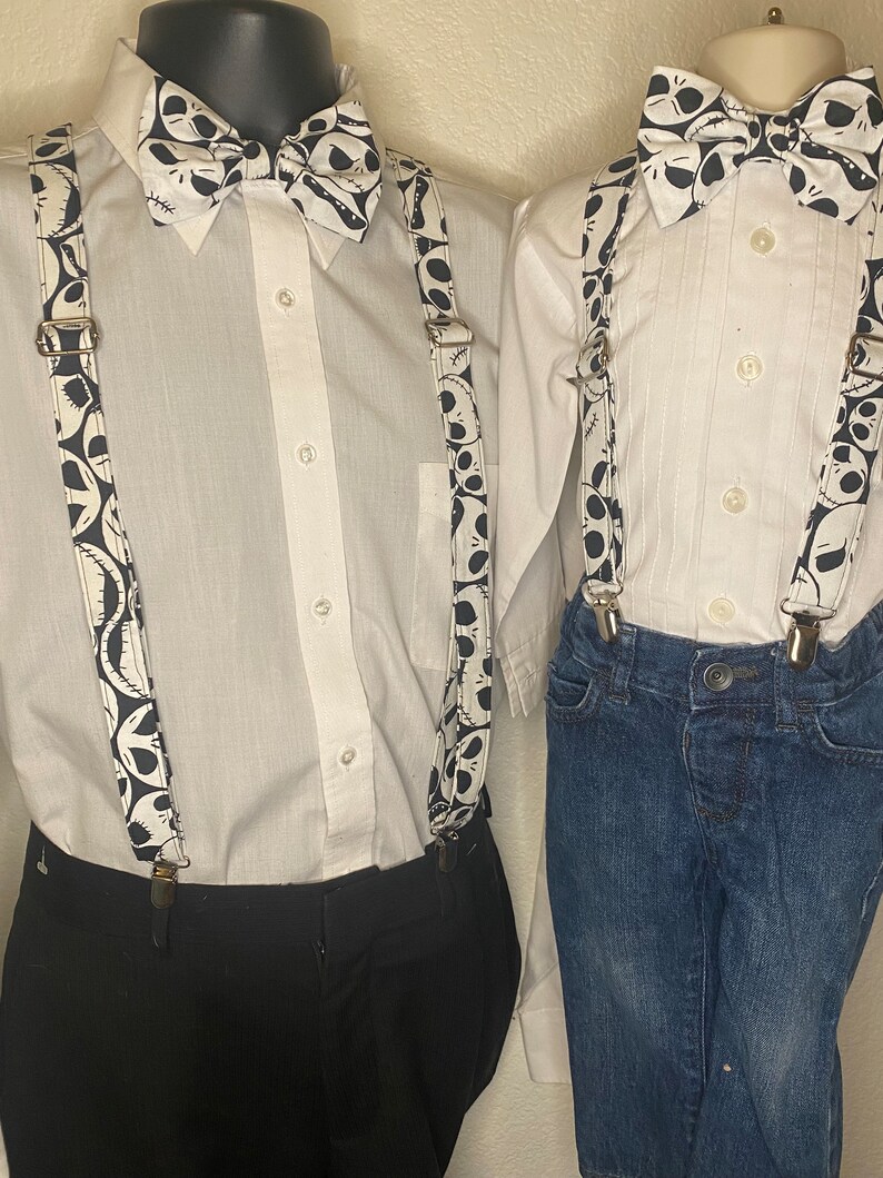 May include: Two white button-down shirts with black and white bow ties and suspenders featuring a Jack Skellington pattern. The suspenders are attached to black pants and blue jeans.