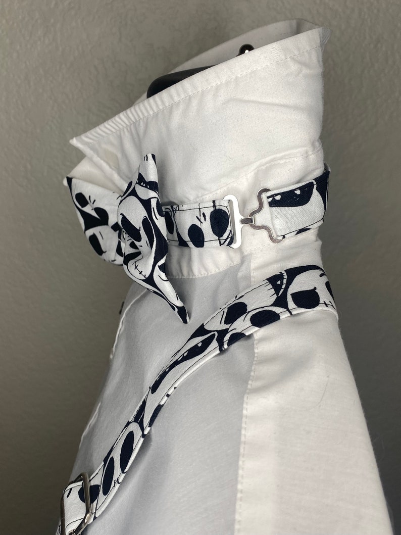 May include: White dress shirt with a black and white bow tie and matching suspenders. The bow tie and suspenders feature a pattern of cartoon skulls.