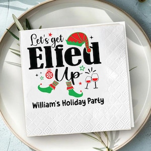 May include: White square paper napkin with the text "Let's get Elfed Up" in black, with festive illustrations of an elf hat, elf shoes, and wine glasses. The text "William's Holiday Party" is below the main text. The napkin is on a white plate.
