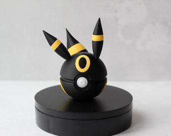 May include: Black and yellow Pokemon figurine of a dark type Eevee evolution. The figurine is in a ball shape with a white circle on the front.