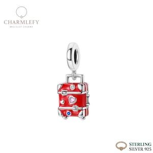 Puede incluir: Un charm de plata de ley con forma de maleta roja con detalles plateados. El charm de maleta tiene una gema en forma de corazón y una gema azul. El charm cuelga de un lazo plateado. La marca "Charmlefy" es visible.
