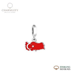 Puede incluir: Un charm de plata con la forma de Turquía en esmalte rojo, con un diseño de luna creciente y estrella blancas. El charm cuelga de un lazo plateado, ideal para pulseras. La marca "Charmlefy" es visible.