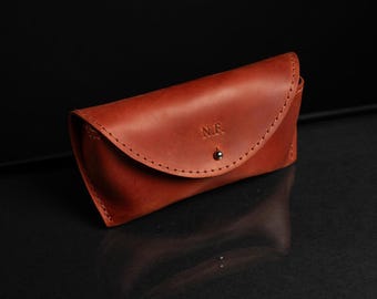 May include: A brown leather glasses case with a snap closure and the initials "M.F." embossed on the front.