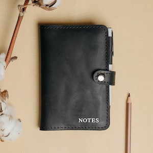 May include: A black leather notebook with a silver button closure and the word "NOTES" embossed on the front.