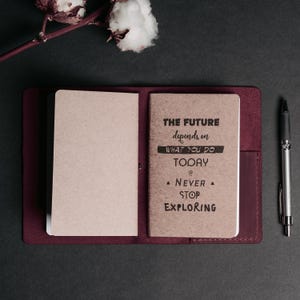 May include: A burgundy leather journal with a brown paper insert. The insert has the text "The future depends on what you do today. Never stop exploring." printed on it.