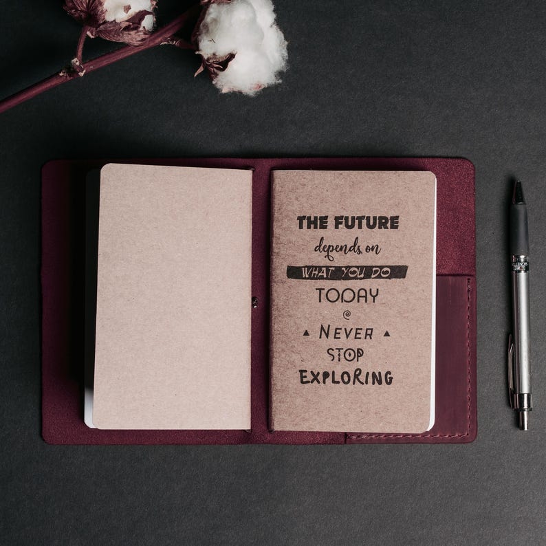 May include: A burgundy leather journal with a brown paper insert. The insert has the text "The future depends on what you do today. Never stop exploring." printed on it.