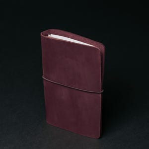 May include: A burgundy leather notebook with a band to keep it closed.