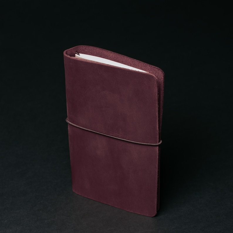 May include: A burgundy leather notebook with a band to keep it closed.
